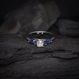 Anillo de compromiso con diamante natural central de .30ct con certificación GIA y 2 zafiros naturales realizado en oro blanco de 18 kilates