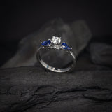 Anillo de compromiso con diamante natural central de .30ct corte brillante con certificación GIA y 2 zafiros naturales realizado en oro blanco de 14k