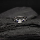 Anillo de compromiso con diamante natural de .20ct corte brillante y 2 zafiros naturales laterales elaborado en oro blanco de 14k