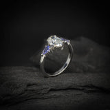 Anillo de compromiso con diamante de laboratorio de 1.0ct corte oval con certificado IGI y 2 tanzanitas naturales laterales elaborado en oro blanco de 14k