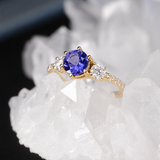 Anillo de compromiso con tanzanita natural de .80ct corte brillante y 12 moissanitas laterales elaborado en oro amarillo de 14k