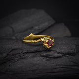 Anillo de compromiso con rubí natural central corte brillante, esmeraldas naturales y diamantes negros  naturales laterales elaborado en oro amarillo de 14k