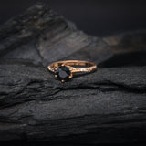 Anillo de compromiso con diamante negro natural central de .70ct y cristales laterales elaborado en oro rosa de 14 kilates