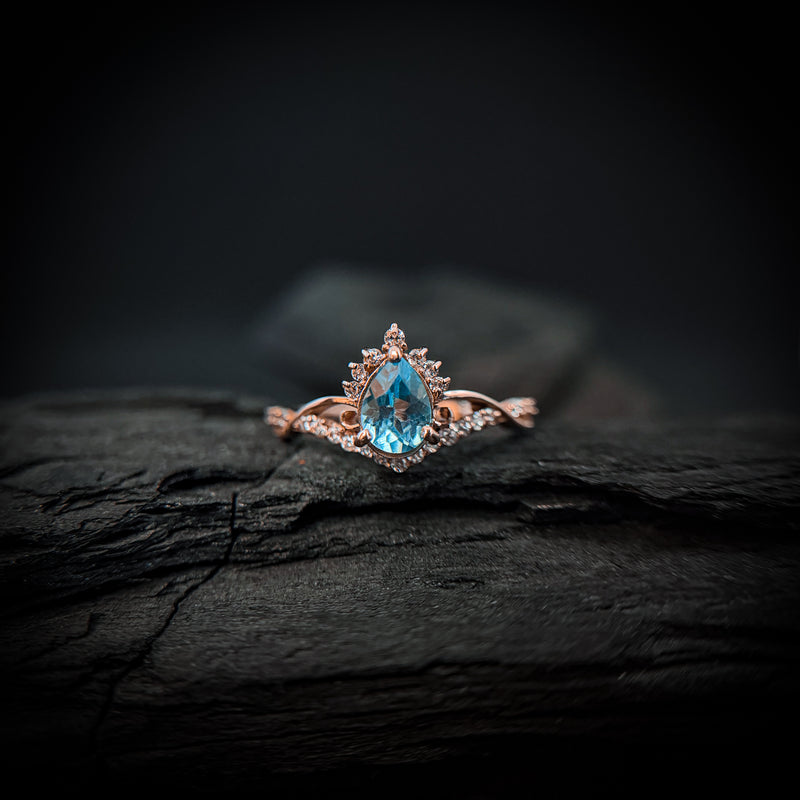 Anillo de compromiso con topacio natural de .80ct corte gota y diamantes naturales laterales elaborado en oro rosa de 14k