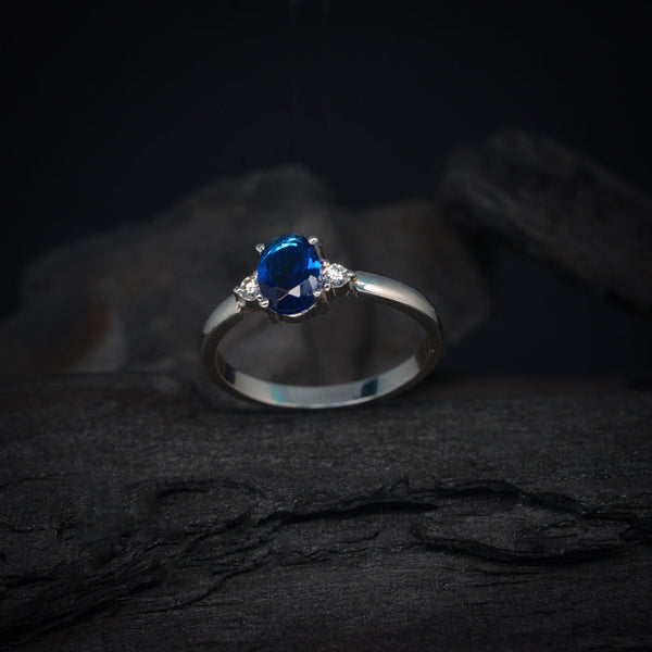 Anillo de compromiso con cristal azul y 2 diamantes laterales elaborado en oro blanco de 18 kilates