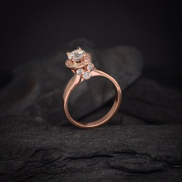 Anillo de compromiso con moissanita de .50ct y cristales laterales elaborado en oro rosa de 14 kilates