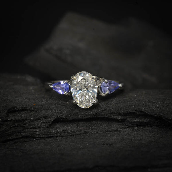 Anillo de compromiso con diamante de laboratorio de 1.0ct corte oval con certificado IGI y 2 tanzanitas naturales laterales elaborado en oro blanco de 14k