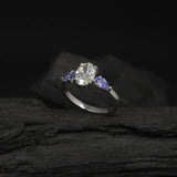 Anillo de compromiso con diamante de laboratorio de 1.0ct corte oval con certificado IGI y 2 tanzanitas naturales laterales elaborado en oro blanco de 14k