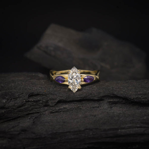 Anillo de compromiso con diamante natural de .70ct corte marquise con certificación GIA y 2 zafiros morados naturales laterales elaborado en oro amarillo de 14k
