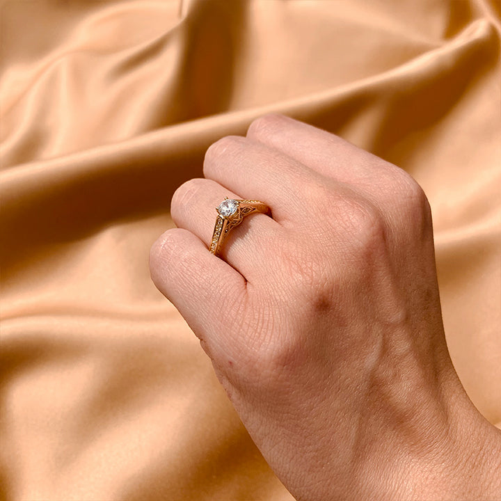 Anillo de compromiso con moissanita de .50ct y cristales laterales elaborado en oro amarillo de 14 kilates