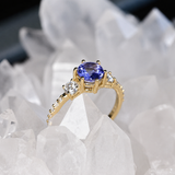 Anillo de compromiso con tanzanita natural de .80ct corte brillante y 12 moissanitas laterales elaborado en oro amarillo de 14k