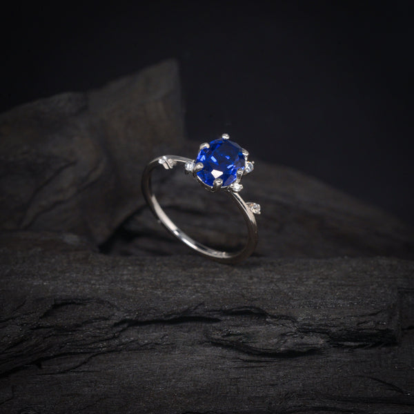 Anillo de compromiso con cristal azul y cristales laterales elaborado en oro blanco de 14 kilates