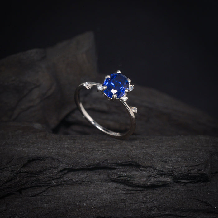 Anillo de compromiso con cristal azul y cristales laterales elaborado en oro blanco de 14 kilates