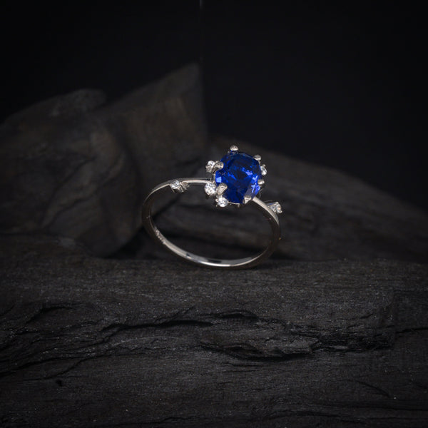 Anillo de compromiso con cristal azul y cristales laterales elaborado en oro blanco de 14 kilates