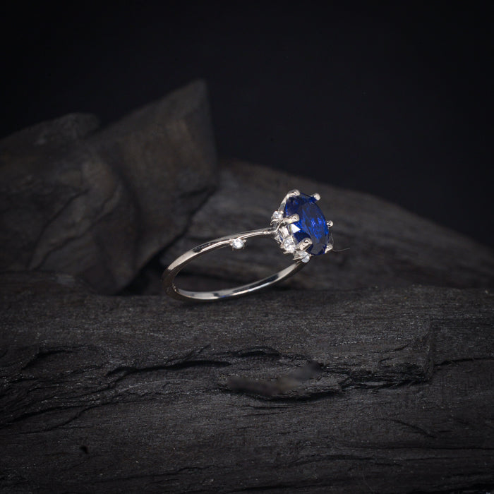 Anillo de compromiso con cristal azul y cristales laterales elaborado en oro blanco de 14 kilates