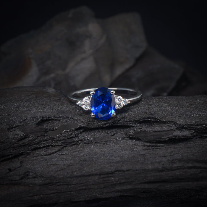 Anillo de compromiso con cristal azul y cristales laterales elaborado en oro blanco de 14 kilates