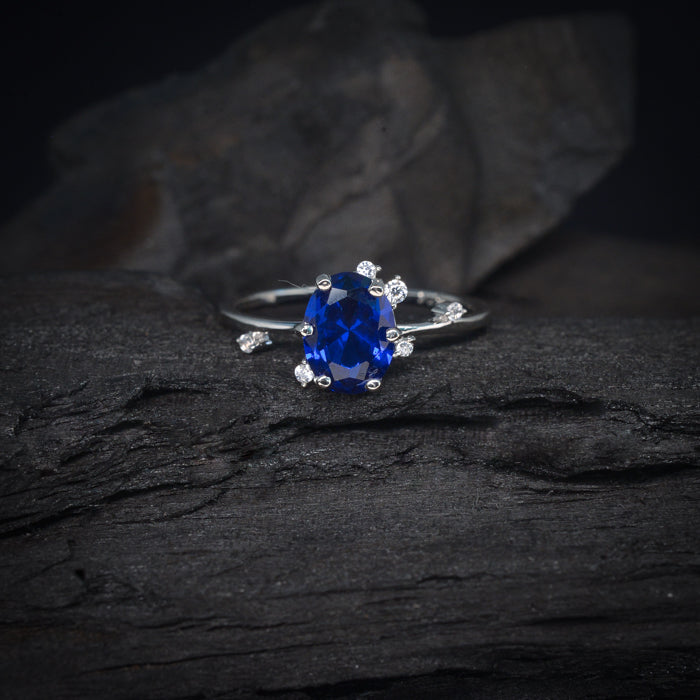 Anillo de compromiso con cristal azul y cristales laterales elaborado en oro blanco de 14 kilates