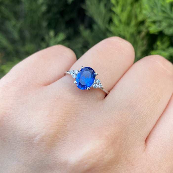Anillo de compromiso con cristal azul y cristales laterales elaborado en oro blanco de 14 kilates