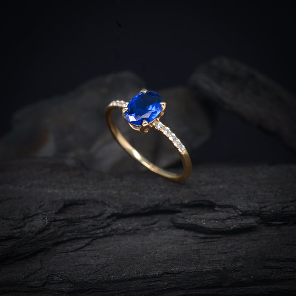 Anillo de compromiso con cristal azul y cristales laterales elaborado en oro amarillo de 14 kilates
