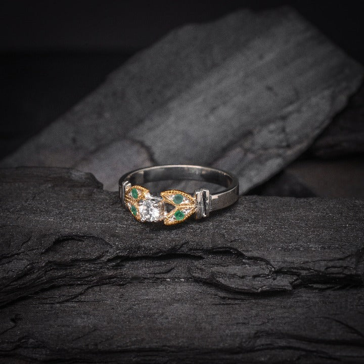 Anillo de compromiso con diamante natural de .15ct y esmeraldas laterales elaborado en oro amarillo y blanco de 14 kilates
