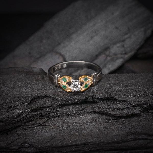 Anillo de compromiso con diamante natural de .15ct y esmeraldas laterales elaborado en oro amarillo y blanco de 14 kilates