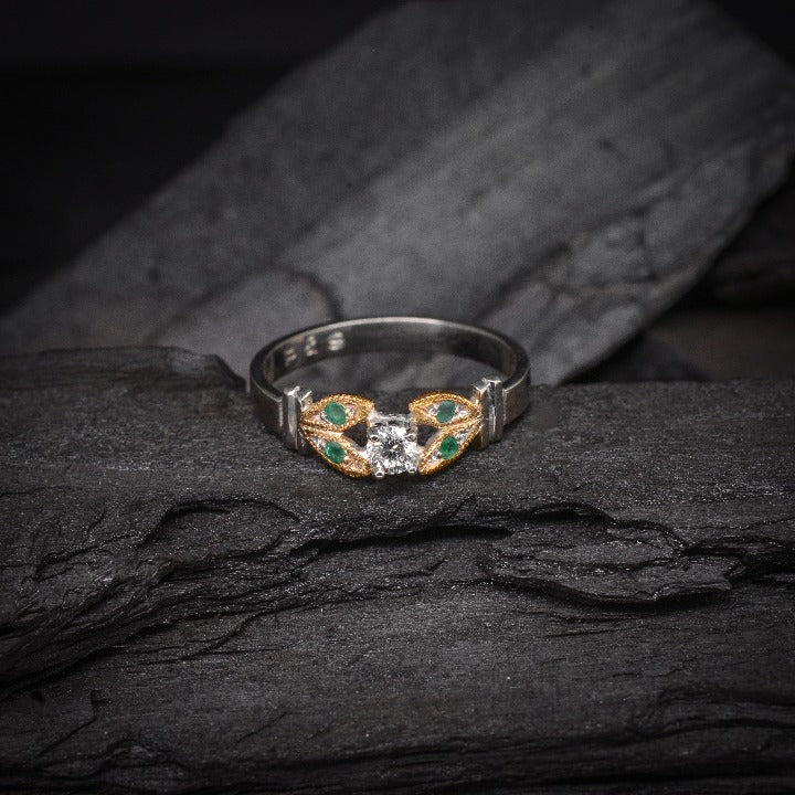 Anillo de compromiso con diamante natural de .15ct y esmeraldas laterales elaborado en oro amarillo y blanco de 14 kilates