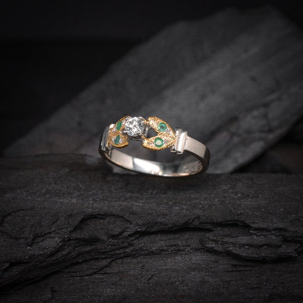 Anillo de compromiso con diamante natural de .15ct y esmeraldas laterales elaborado en oro amarillo y blanco de 14 kilates