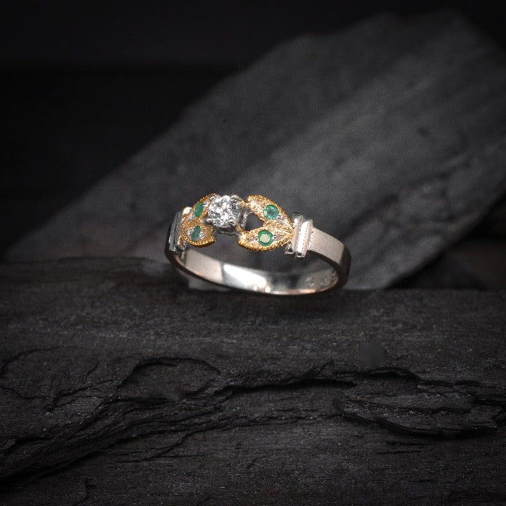 Anillo de compromiso con diamante natural de .15ct y esmeraldas laterales elaborado en oro amarillo y blanco de 14 kilates