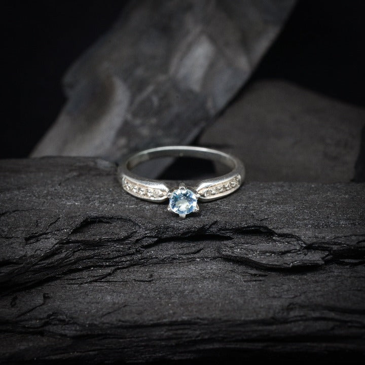 Anillo de compromiso con topacio natural y cristales laterales realizado en oro blanco de 14 kilates