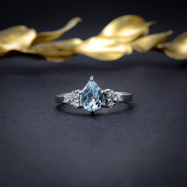 Anillo de compromiso con topacio corte gota y 6 diamantes laterales en oro blanco de 14 kilates