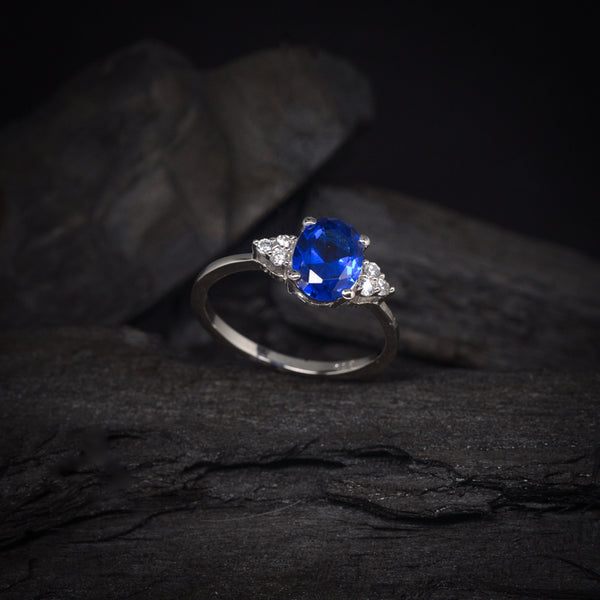 Anillo de compromiso con cristal azul y cristales laterales elaborado en oro blanco de 14 kilates