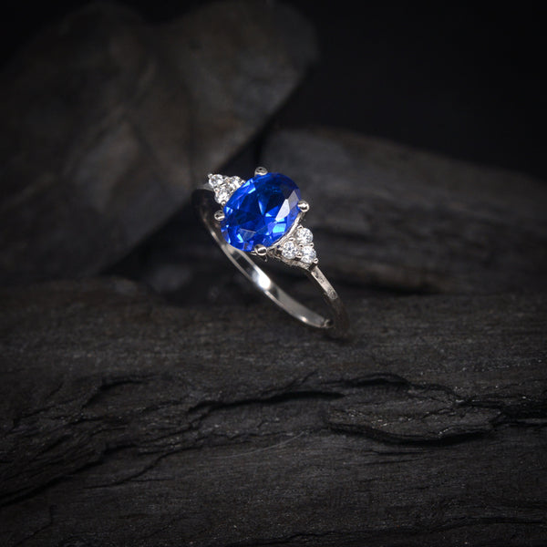Anillo de compromiso con cristal azul y cristales laterales elaborado en oro blanco de 14 kilates