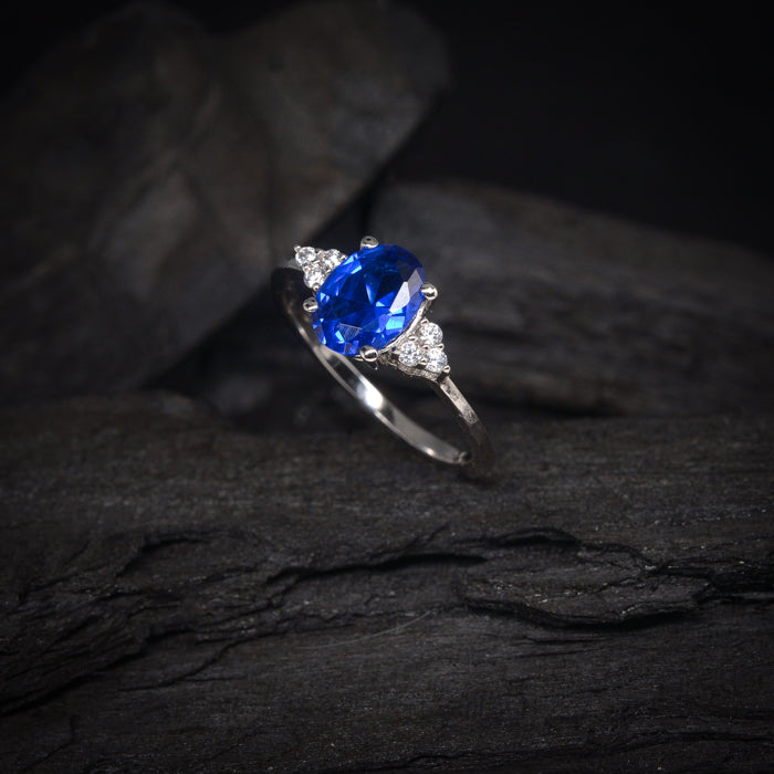 Anillo de compromiso con cristal azul y cristales laterales elaborado en oro blanco de 14 kilates